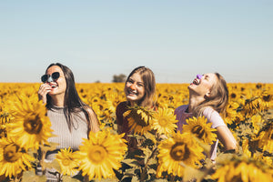 Three cheerful young ladies outside in a sunflower field with Nöz sunscreen on their nose 